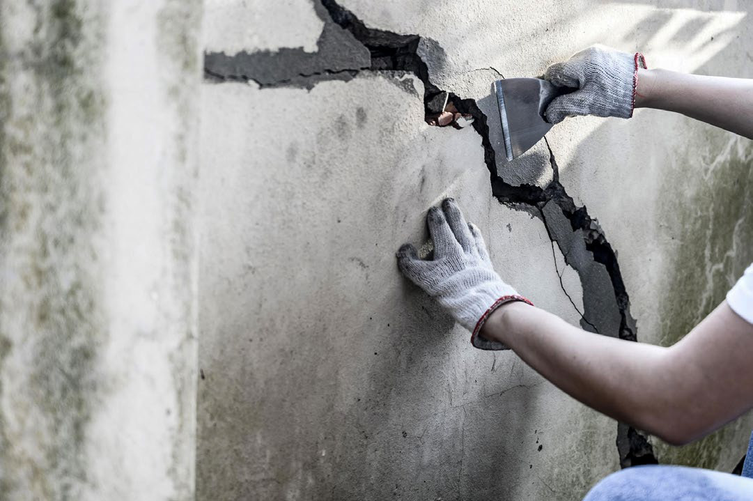 Worker scraping a cracked wall with a putty knife